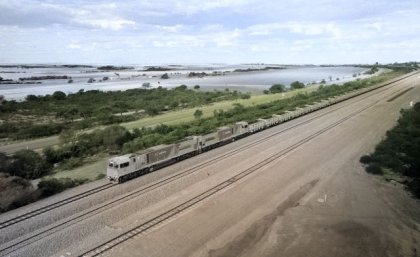 A long train travels on a track with fields and open country either side of it.